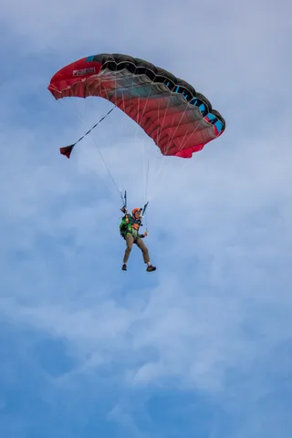 A red canopy carries a skydiver high above the park.