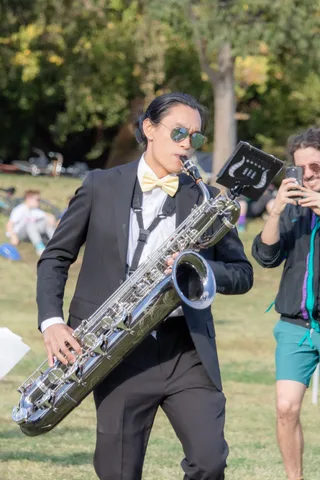 A baritone saxophone player in a tuxedo marches across the grass.