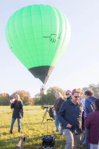 A green balloon sits on the lawn while a crowd watches nearby