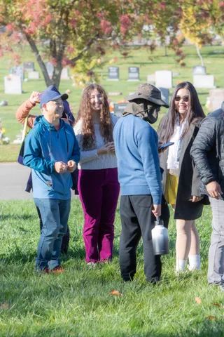 A small group stands talking on the lawn among headstones
