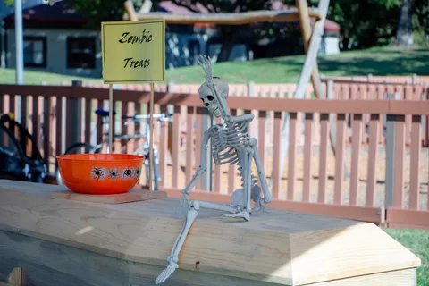 A jointed skeleton and a bowl of candy sit on a wooden coffin under a Zombie Treats sign.