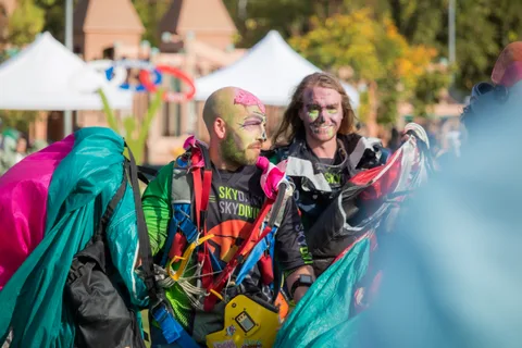 Two skydivers in face paint gather a canopy in front of the tents.