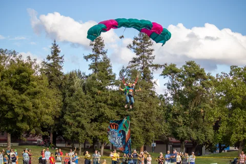 A skydiver glides toward the crowd lining the edge of the field.