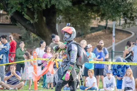 A skydiver in helmet and face paint walks past the caution tape.