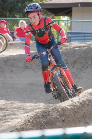 A BMX rider in full kit carves through a berm on the dirt track.