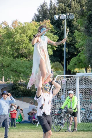 A performer in a pale gown balances on someone's shoulders high above the field.