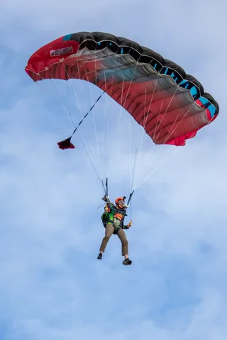 A skydiver steers a red canopy through thin cloud.