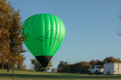 A green balloon stands inflated beside the trees