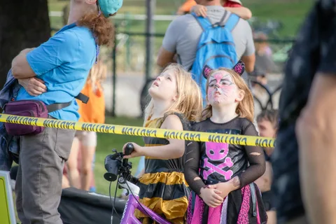 Two children in Halloween costumes look up from behind the caution tape.
