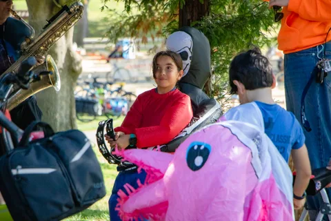 A band member plays a tambourine beside a child in an inflatable costume.