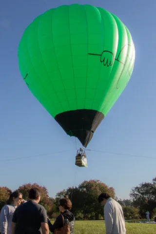 A green balloon lifts off above a group watching from the grass