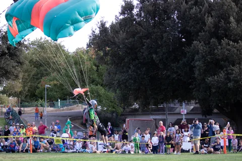A skydiver lands on the grass as families watch from the tape.