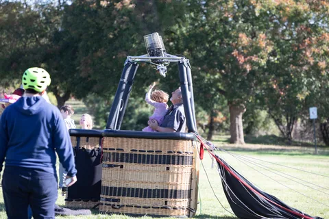 A child waves from a balloon basket resting on the grass