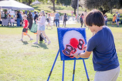 A child throws a soft ball at a painted target board on the grass.