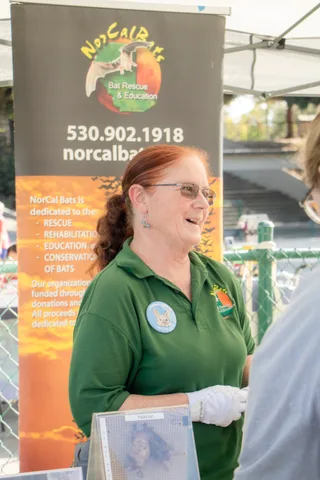 A bat rescue volunteer talks with visitors in front of a NorCal Bats banner.