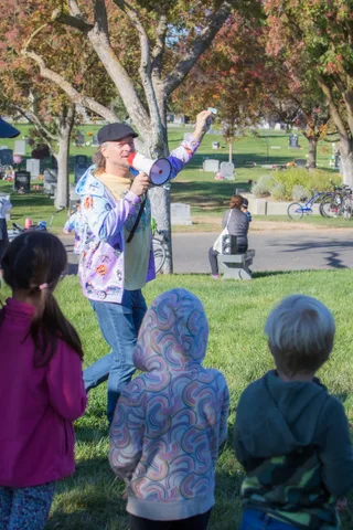 A person with a megaphone speaks to children on the grass