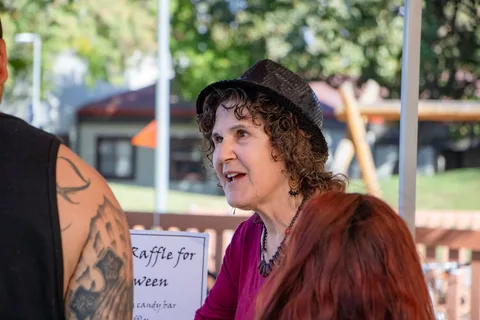 A visitor in a hat and feather boa chats beside a raffle sign.