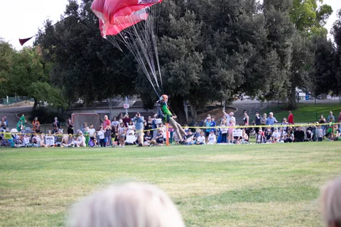 A skydiver skims in over the grass past a line of spectators.