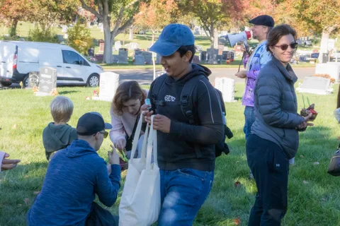 People gather on the grass with tote bags on a sunny morning
