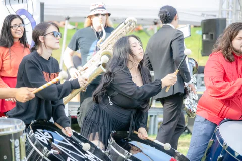 The drum line plays while a saxophone player leans into the tune behind them.