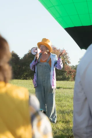A person in overalls and a straw hat speaks into a megaphone