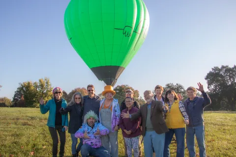 People wave on the grass as a green balloon rises behind