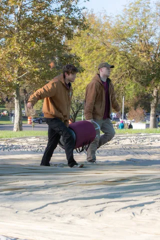 Two people carry a rolled balloon envelope across a tarp