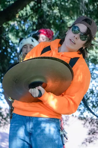 A cymbal player in an orange hoodie crashes cymbals during the parade.