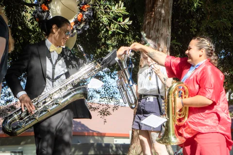 A baritone saxophone player in a tailcoat plays beside a bandmate in red.