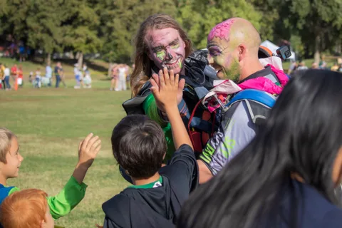 Two skydivers in face paint greet children at the tape line.