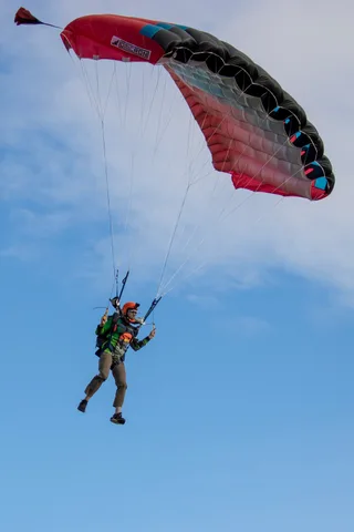 A skydiver leans into a turn beneath the red canopy.