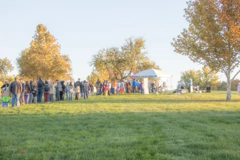 A long line of people waits across the lawn