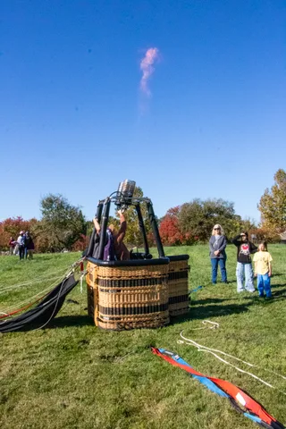 A hot air balloon basket sits on the grass under a clear blue sky.