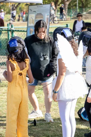 Two children in fencing masks wait their turn beside a friend in angel wings.