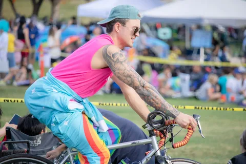 A cyclist in a bright pink tank top and rainbow-striped pants rides past caution tape at the Zombie Bike Parade festival