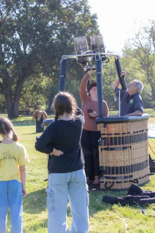 People stand beside a balloon basket on the grass