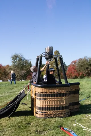 A balloon basket and burners stand upright on the grass.