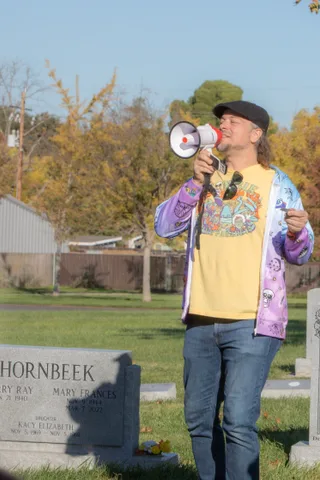 A person with a megaphone speaks at a grassy gathering