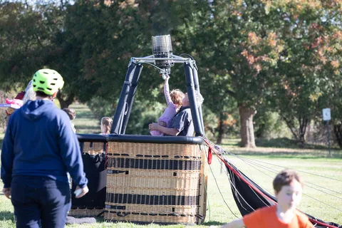 A child sits in a balloon basket while an adult looks on