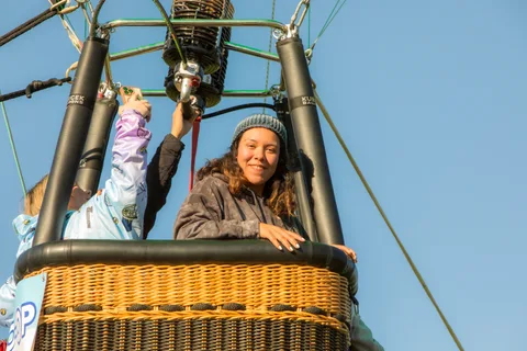 A passenger leans out of a balloon basket against the sky
