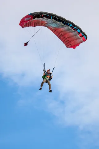 A skydiver drops toward the field under a red canopy.