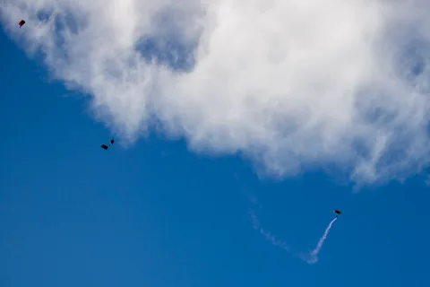 A smoke trail marks a skydiver's descent across a clear blue sky.