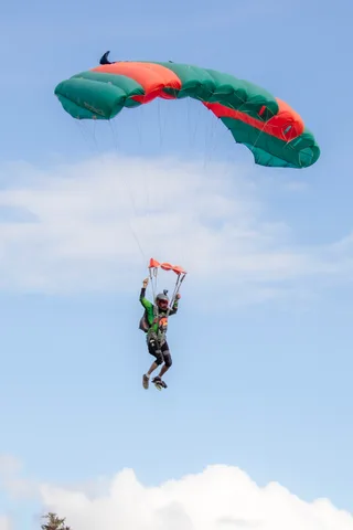 A green and orange canopy glides beneath drifting clouds.