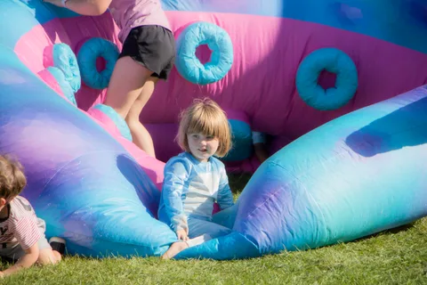 A young child sits in the mouth of the octopus bounce house while others jump behind them.