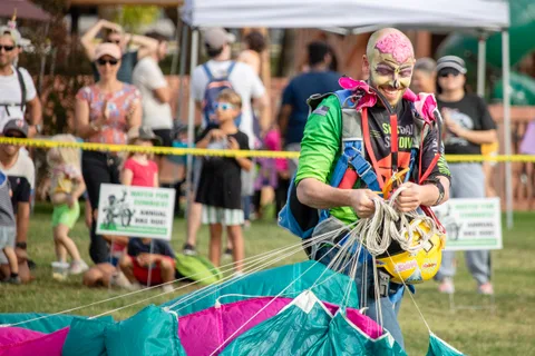 A skydiver in face paint coils lines with the canopy on the grass.