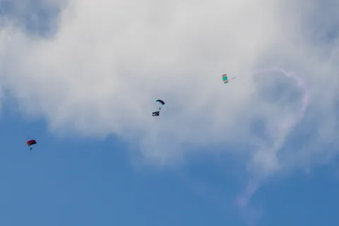 Skydivers leave smoke trails across the cloud and blue sky.