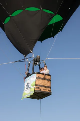 A balloon basket with passengers climbs above the trees