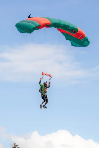 Skydiver descending with an orange and green parachute canopy at the Zombie Bike Parade festival