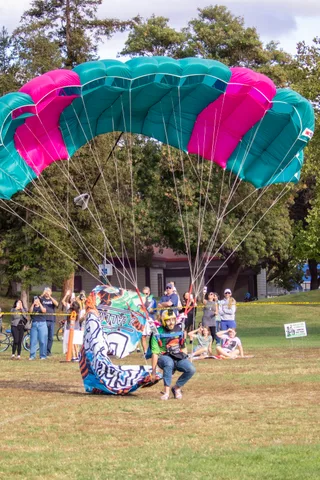 The canopy folds behind a skydiver resting on the grass.