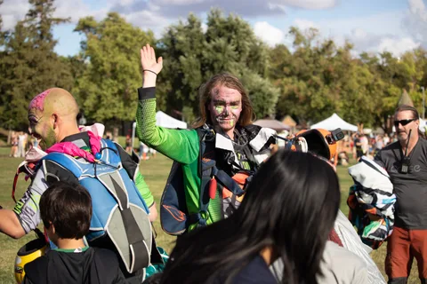 A skydiver waves to the crowd with gear over one shoulder.